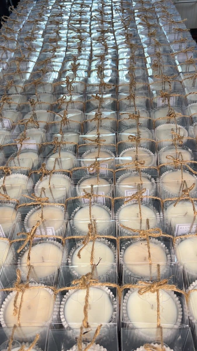Candle favours in clear gift boxes, tied with twine and labelled, ready for guests